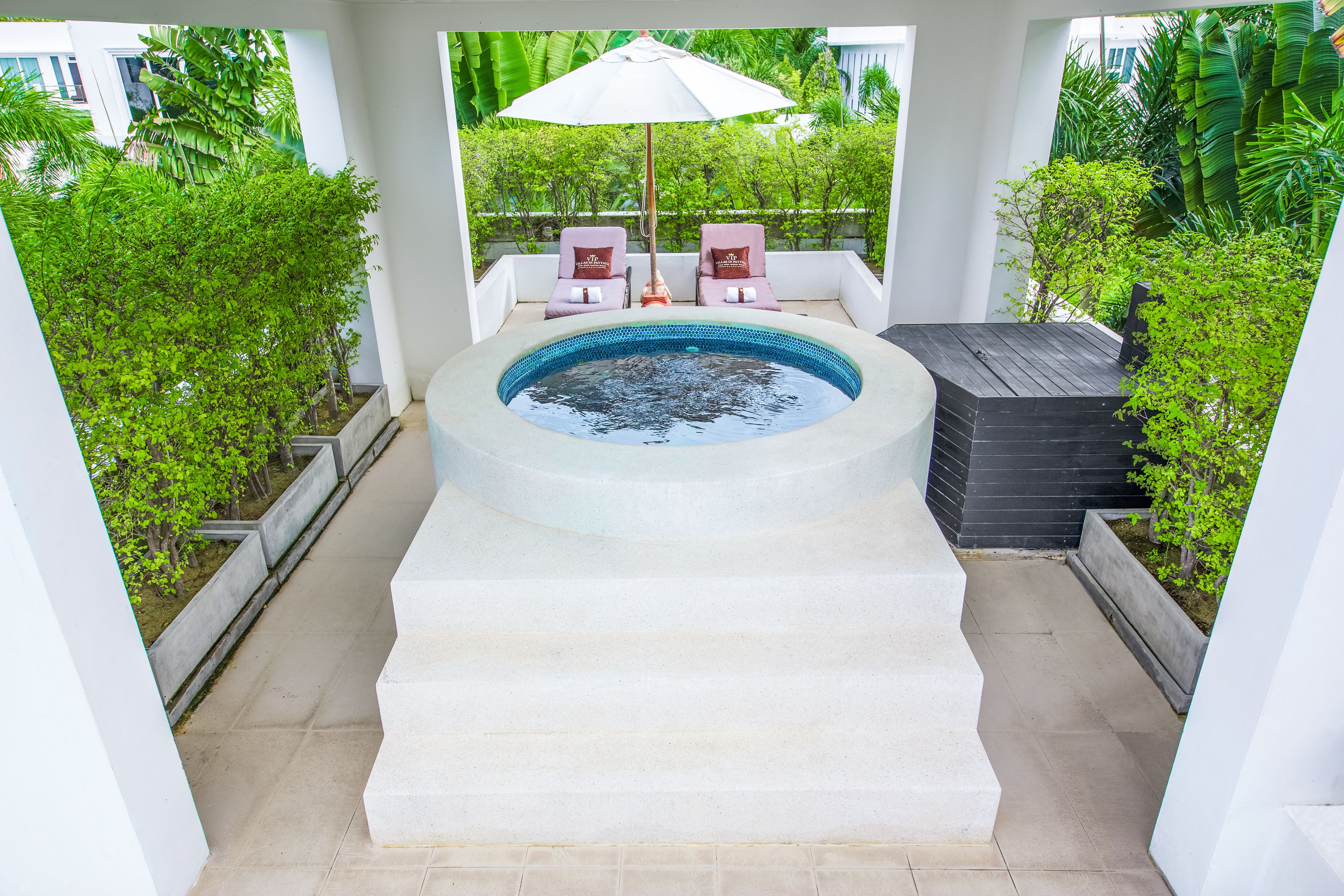 A hot tub with two lounge chairs and an umbrella, surrounded by greenery.
