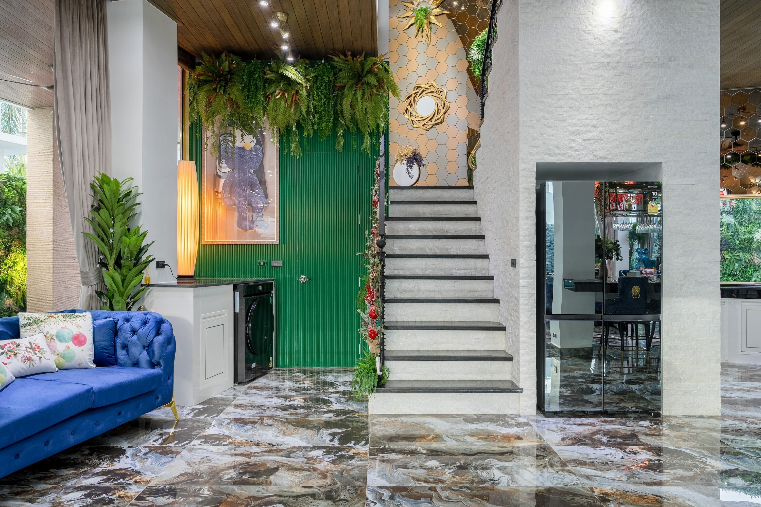 A modern interior with a blue sofa, green door, staircase, and a kitchen area.
