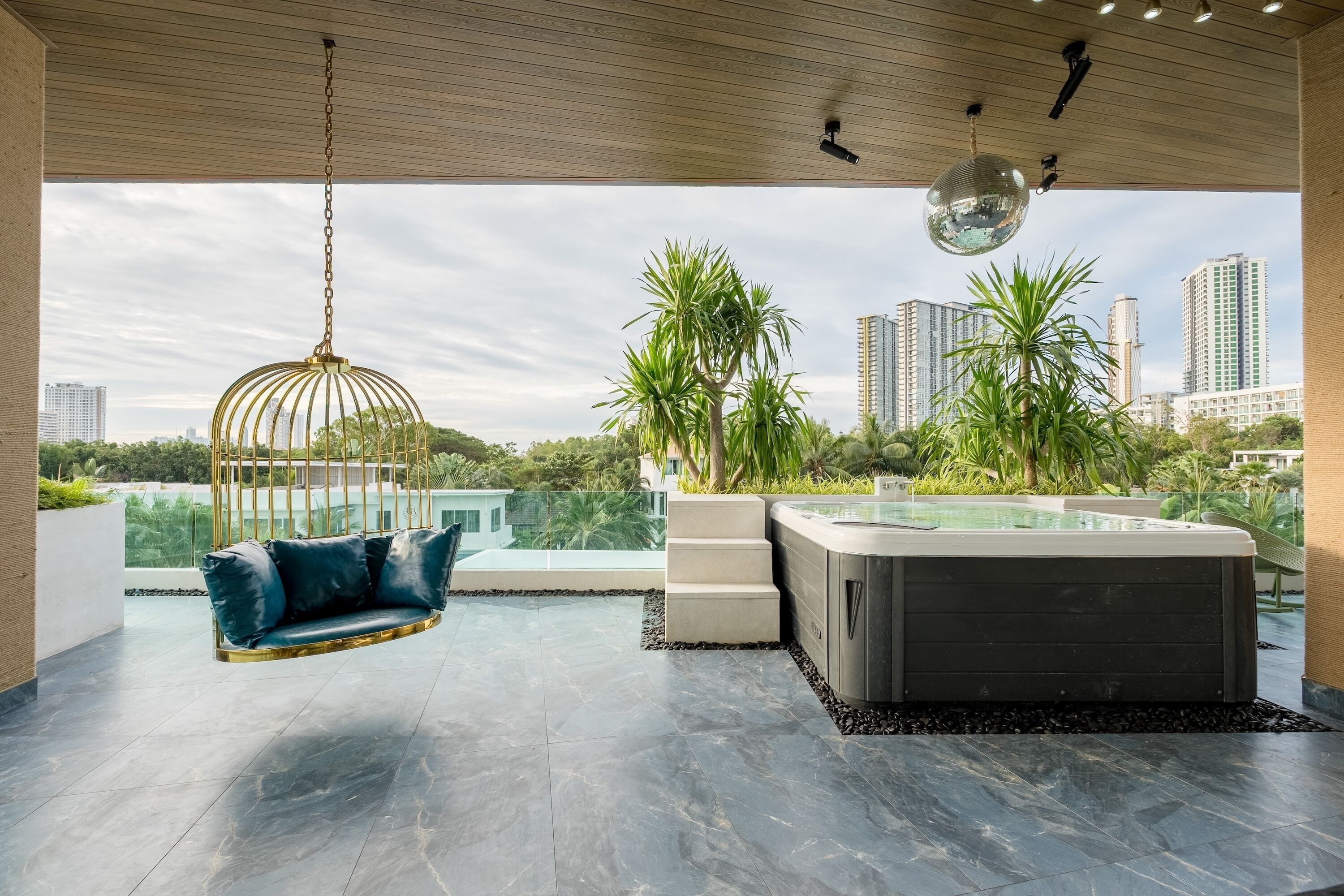 Un espacio lounge moderno al aire libre con una hamaca colgante, un jacuzzi y vistas a un paisaje urbano.