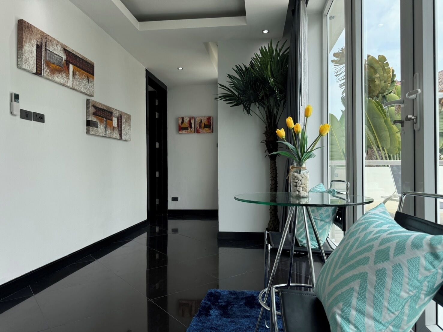 Un interior moderno con una mesa de vidrio, sillas, un jarrón con flores amarillas y obras de arte en las paredes.