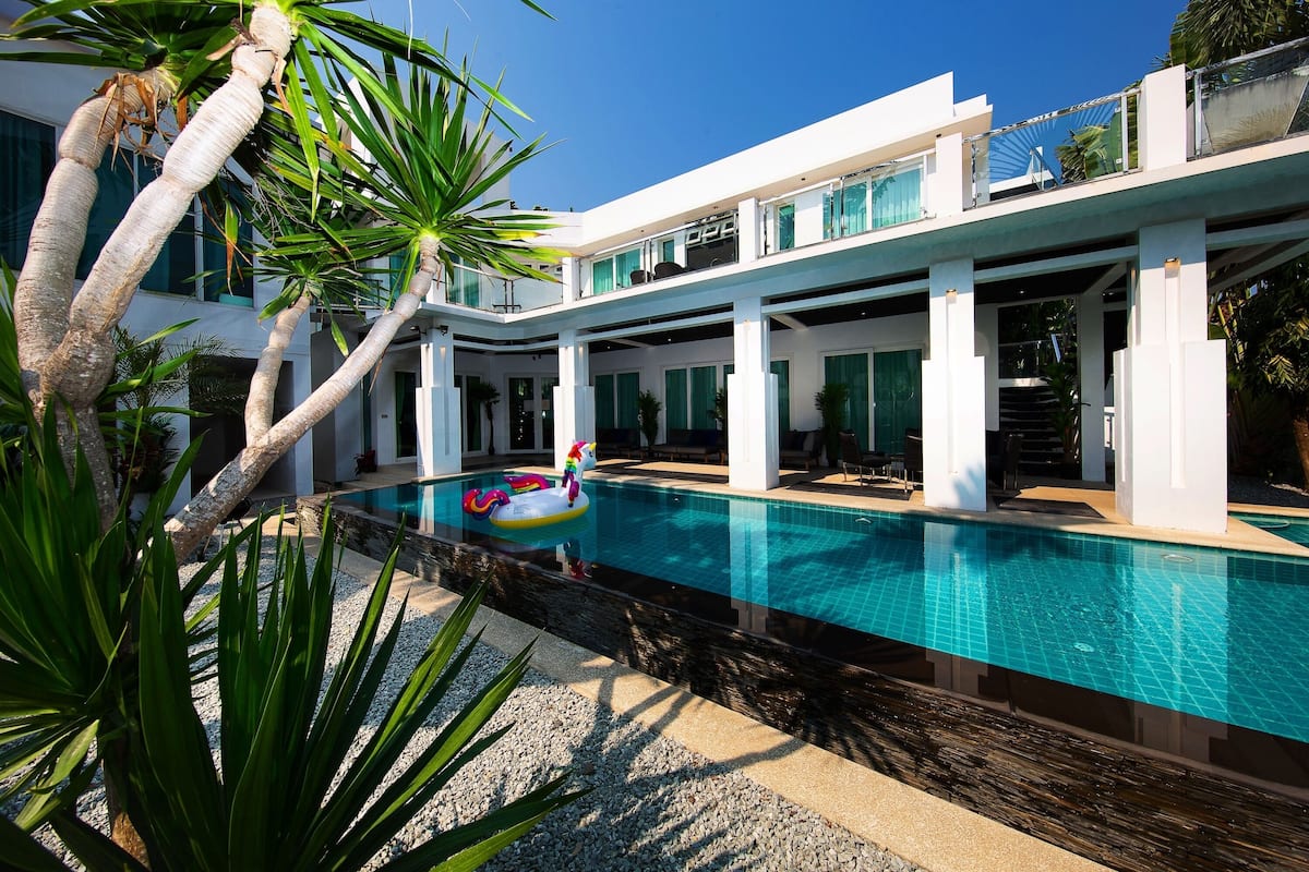 Une maison moderne dotée d’une piscine, de piliers blancs et d’un balcon avec une balustrade en verre.