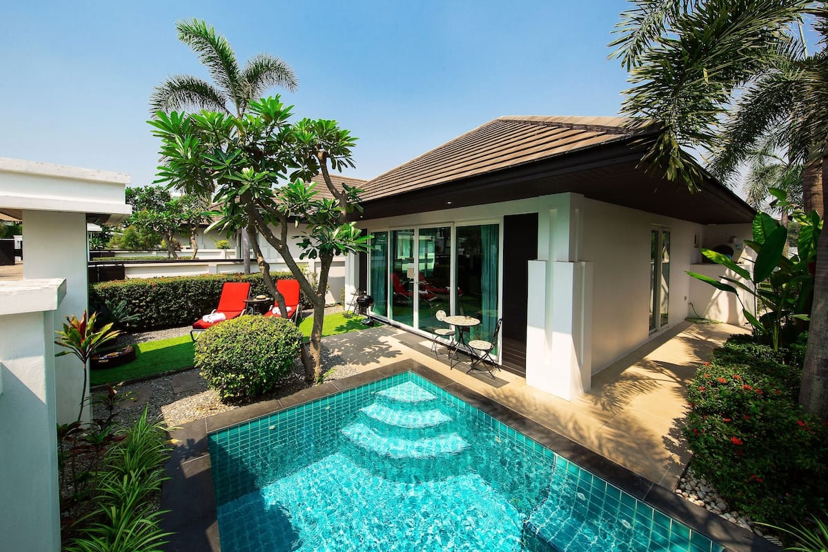 Une maison moderne dotée d’une piscine, de chaises longues rouges et d’une végétation luxuriante.