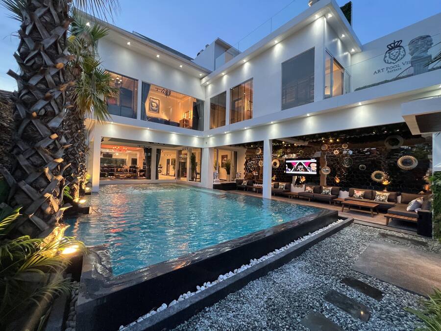 Uma área moderna à beira da piscina, com uma piscina grande, assentos externos e uma entrada bem iluminada.