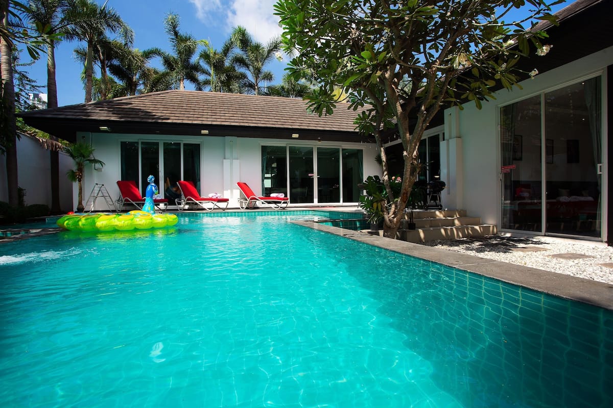Une piscine avec des chaises longues et un arbre en arrière-plan.