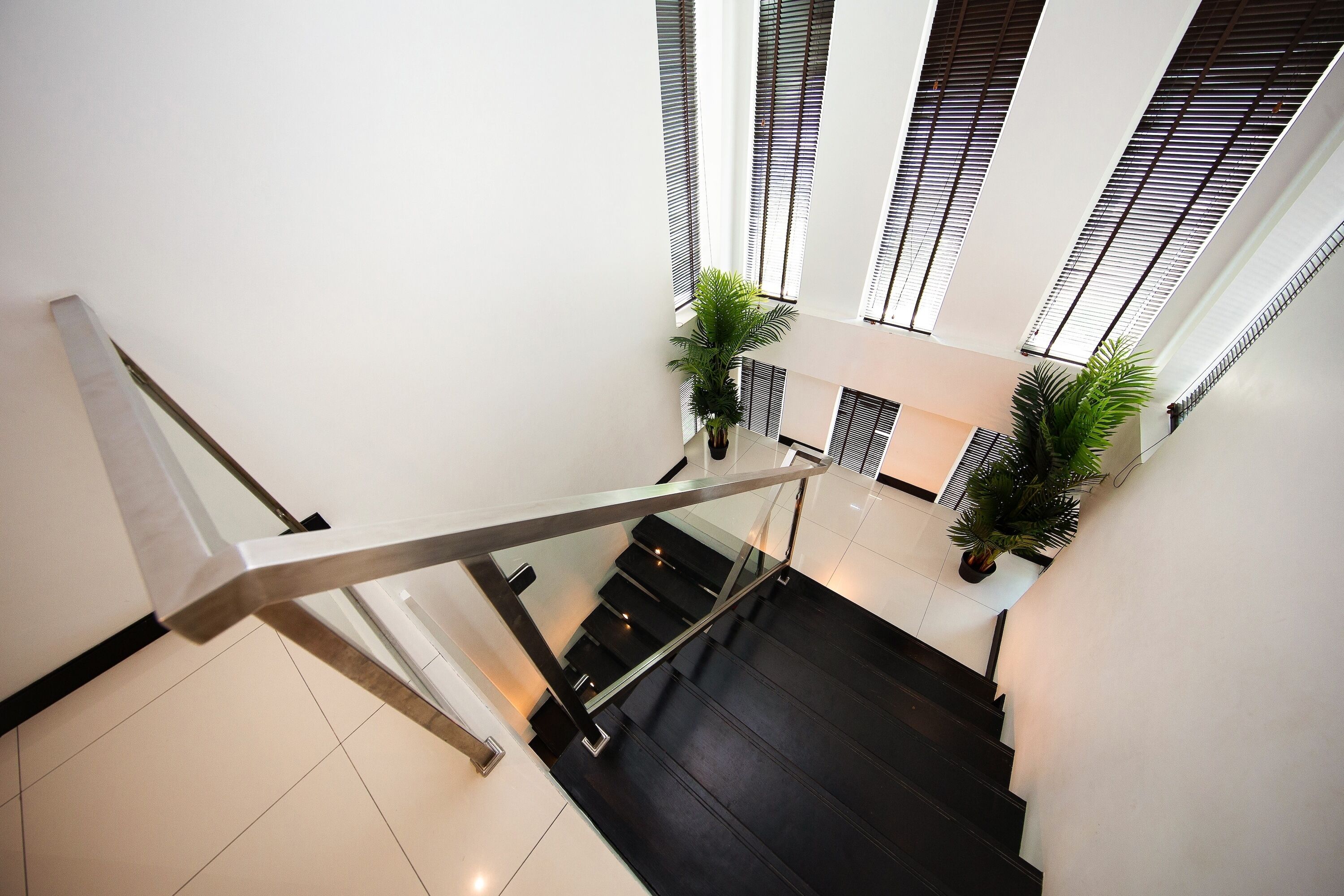Un interior moderno con escalera, barandillas de vidrio y plantas en macetas.
