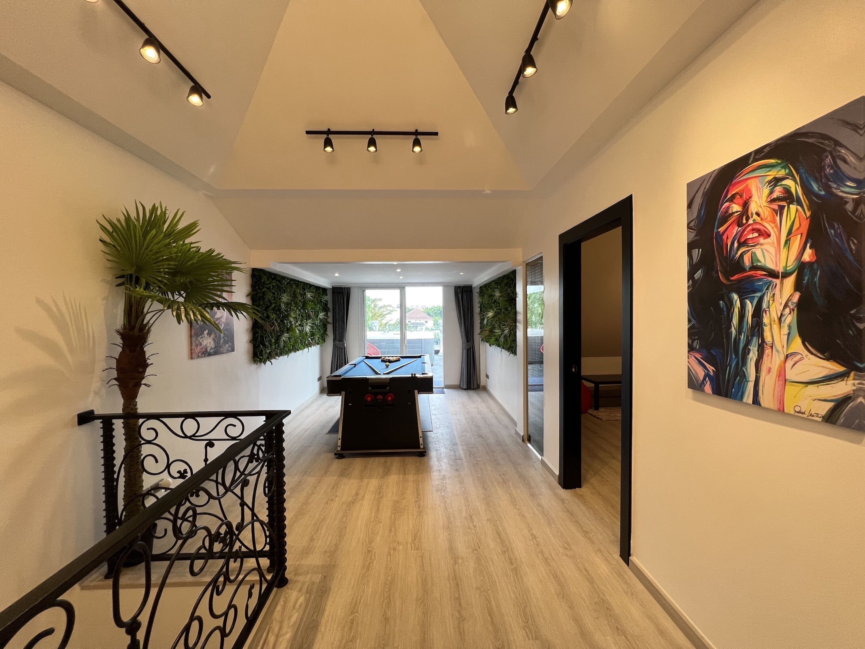 A hallway with a pool table, a staircase with a railing, and a large painting on the wall.