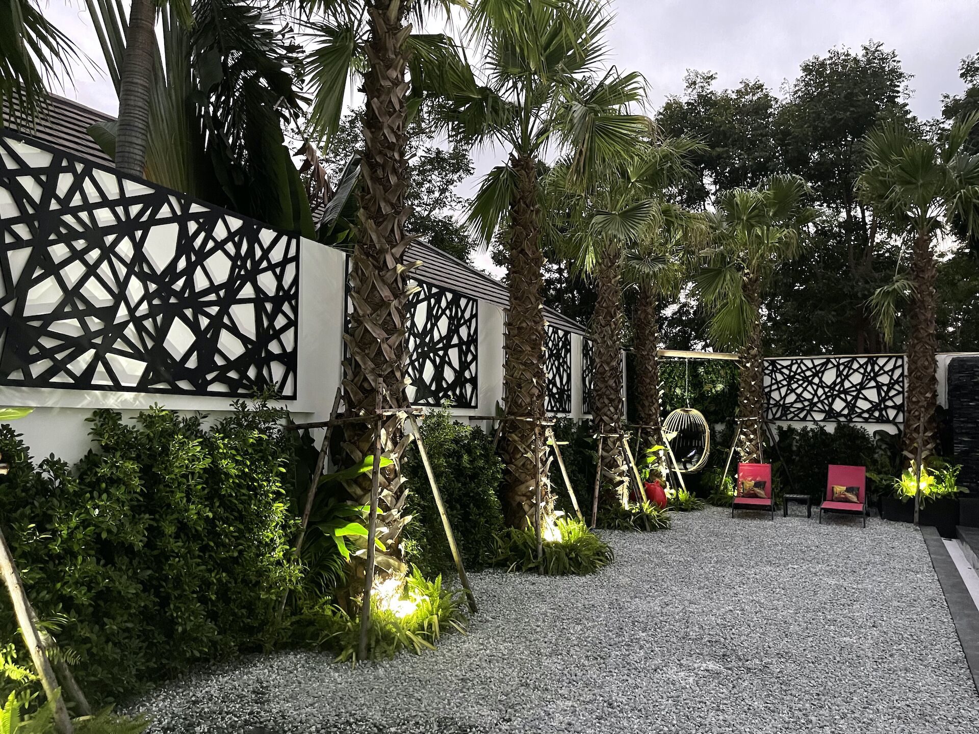 A garden with a gravel path, palm trees, and a decorative fence.