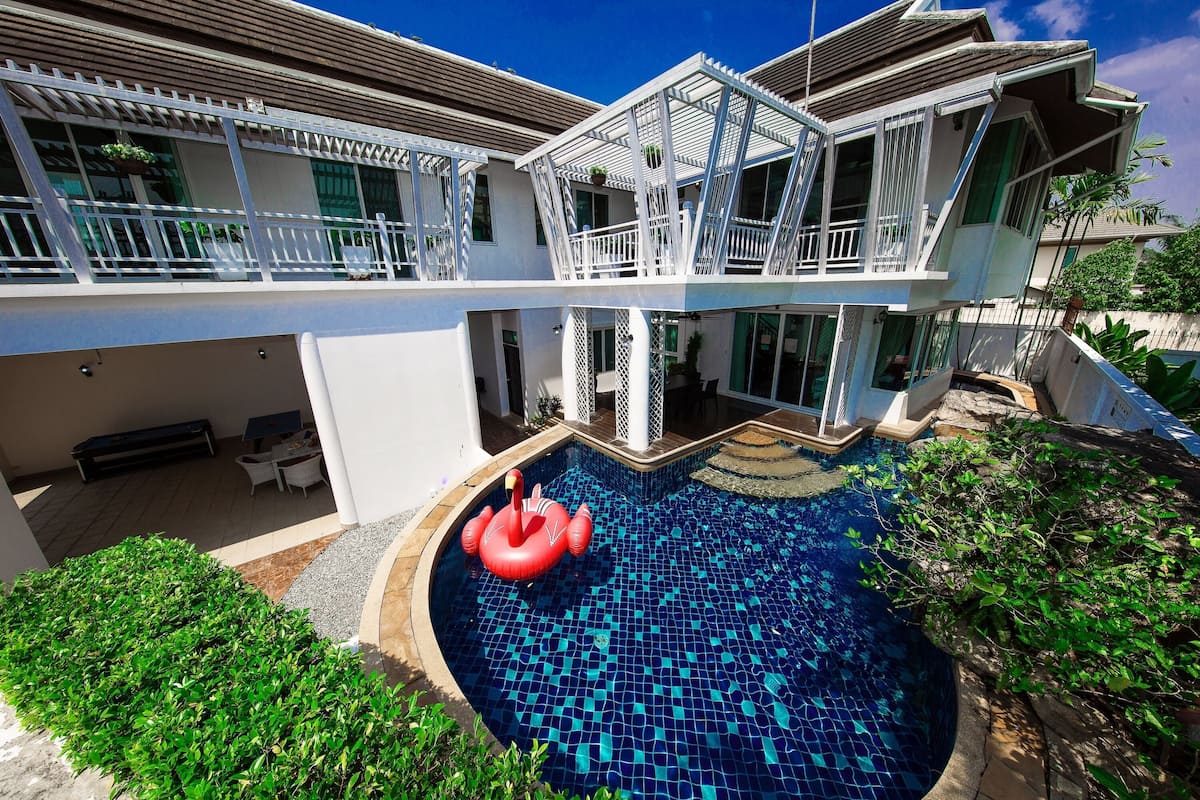 Une maison à deux étages avec une piscine, un balcon blanc et un jardin.