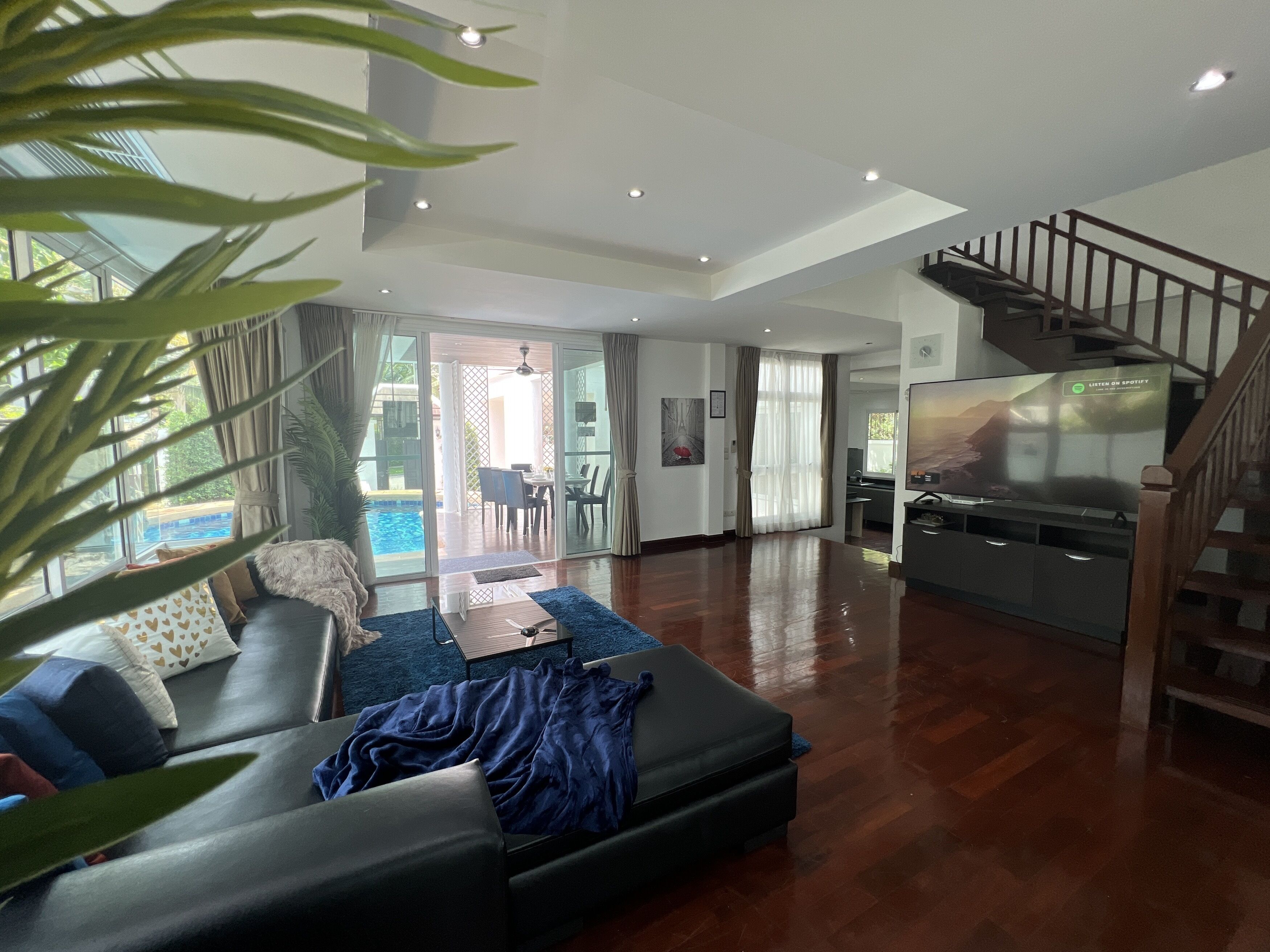 A spacious living room with a large sofa, a coffee table, and a TV. There is a staircase leading to an upper level.