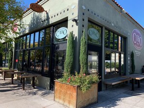 Un bar restaurante CIBO con grandes ventanales, terraza al aire libre y una jardinera con flores.