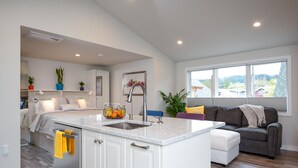 A modern kitchen with a central island, white cabinetry, and a view of the outdoors through large windows. - Jewel in the Sky:   Modern, Private,  Luxurious Loft + EV Charger! (Portland)