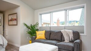 A living room with a gray sofa, a white ottoman, a yellow pillow, and a plant. - Jewel in the Sky:   Modern, Private,  Luxurious Loft + EV Charger! (Portland)