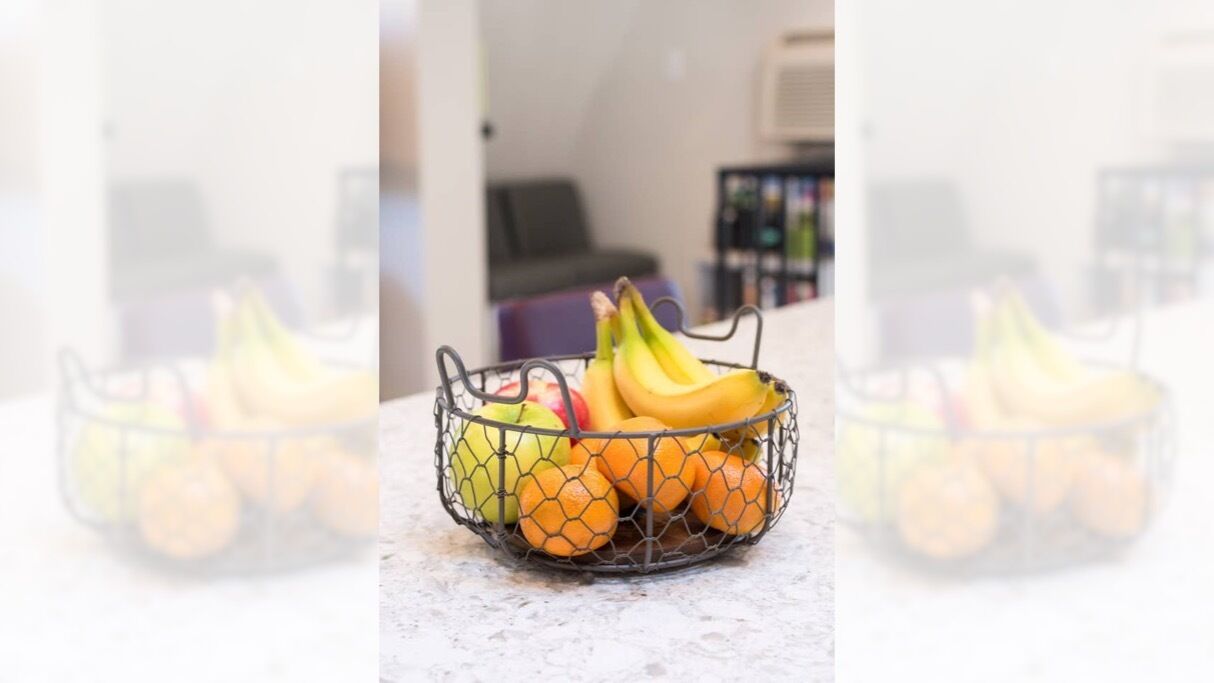 Una cesta de frutas con plátanos y naranjas sobre una encimera de mármol.
