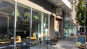 An outdoor seating area with tables and chairs, a glass storefront, and hanging plants. - Jewel in the Sky:   Modern, Private,  Luxurious Loft + EV Charger! (Portland)