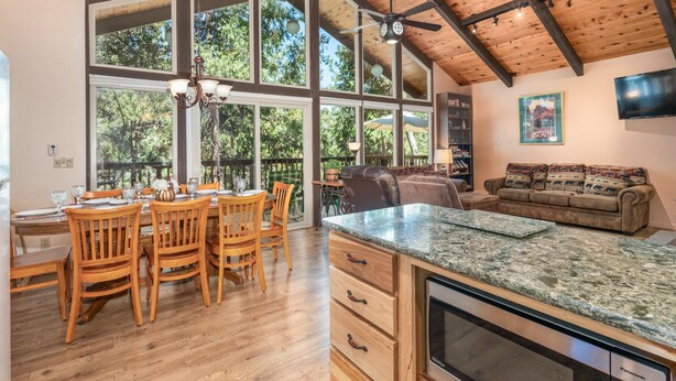 A spacious kitchen with wooden cabinets, a granite countertop, and a large window overlooking a forest. - Cedar Mountain Lodge (Oakhurst)