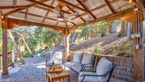 A covered patio with wooden furniture, a swing set, and a view of a wooded area. - Cedar Mountain Lodge (Oakhurst)