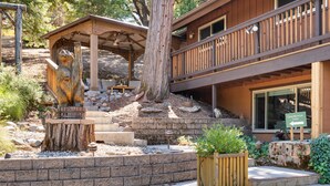 A lodge with a wooden deck, a covered seating area, and a stone staircase leading to the entrance. - Cedar Mountain Lodge (Oakhurst)