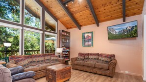 A spacious living room with large windows, a wooden ceiling, and a cozy seating area with a sofa and armchairs. - Cedar Mountain Lodge (Oakhurst)