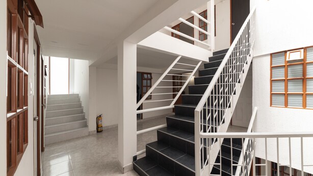 A multi-level interior with a staircase, a fire extinguisher, and a door with a number.