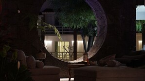 A cozy lounge area with a circular mirror reflecting a tree and a building, surrounded by comfortable seating and a small table with a lamp. - El Laurel Hotel Boutique (Xochitepec)