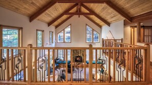 Un intérieur spacieux avec un haut plafond en bois, de nombreuses fenêtres et un escalier doté d’une rampe en bois.