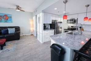 A modern kitchen with a granite countertop, stainless steel appliances, and pendant lighting. - Sunbird 210w-Cozy Beachfront Condo with Sunset Views – Prime PCB Location (Panama City Beach)