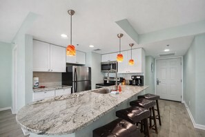 A modern kitchen with a marble countertop, stainless steel appliances, and pendant lighting. - Sunbird 210w-Cozy Beachfront Condo with Sunset Views – Prime PCB Location (Panama City Beach)