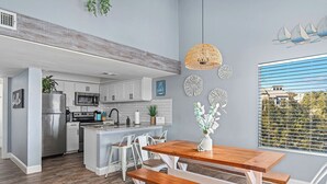A modern kitchen with white cabinets, a stainless steel refrigerator, and a wooden dining table with benches. - Cozy Waterfront/Amazing Views/"Paradise Point" in Point Venture! (Leander)