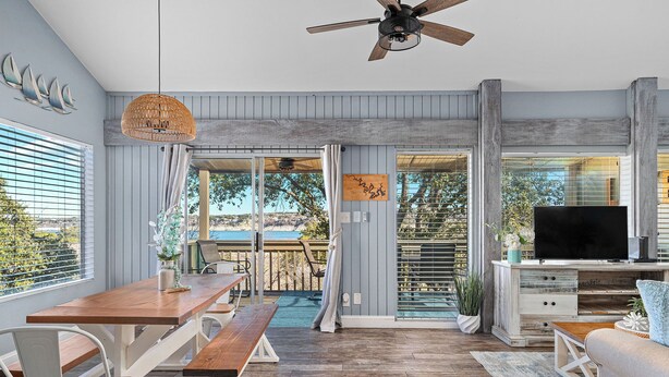 A spacious living area with a wooden dining table, a sofa, and a TV. - Cozy Waterfront/Amazing Views/"Paradise Point" in Point Venture! (Leander)