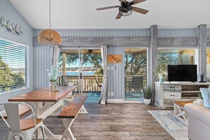 A spacious living area with a wooden dining table, a sofa, and a TV. - Cozy Waterfront/Amazing Views/"Paradise Point" in Point Venture! (Leander)