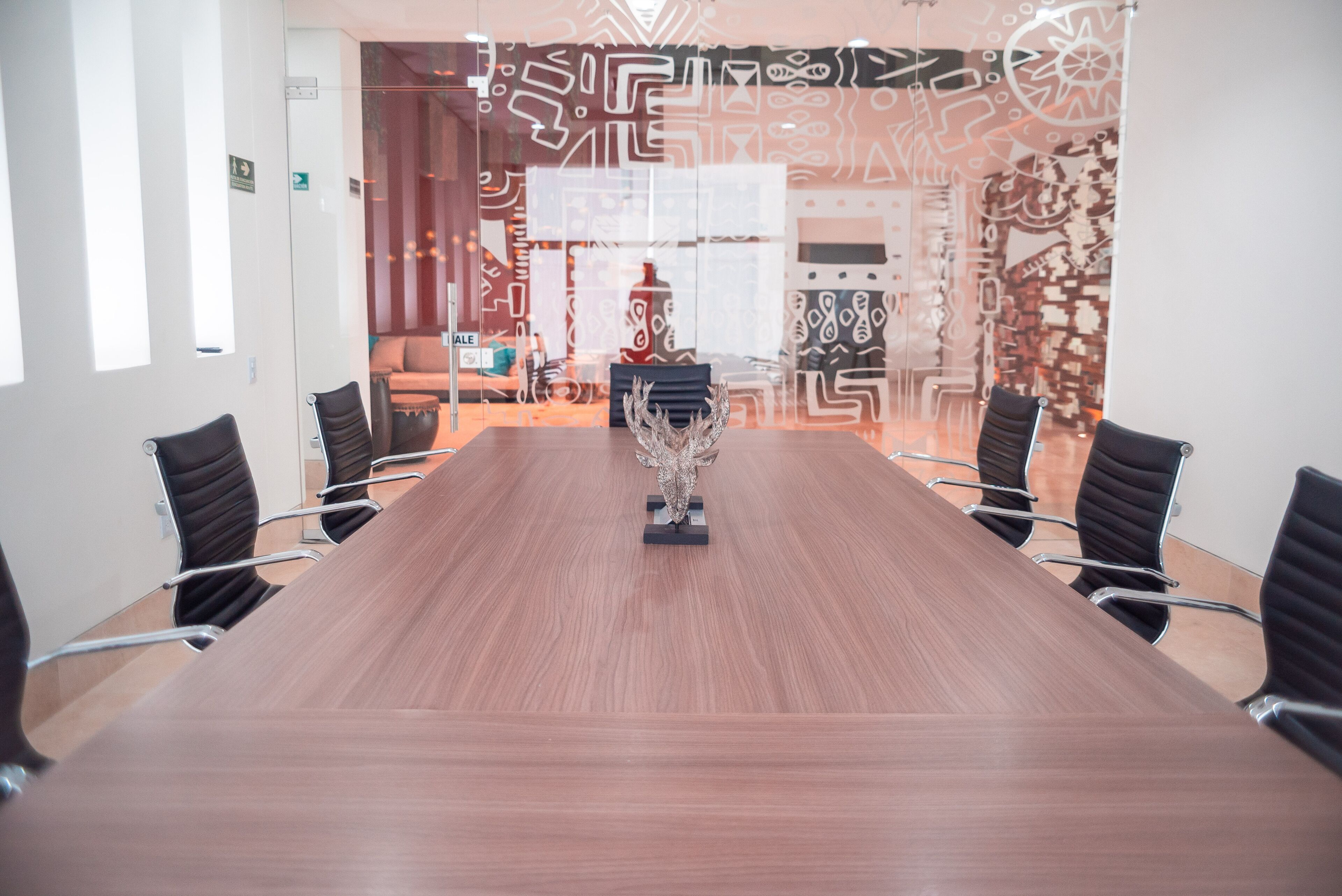 Une salle de conférence avec une longue table et des chaises noires, un élément décoratif mural et un mur à motifs en arrière-plan.