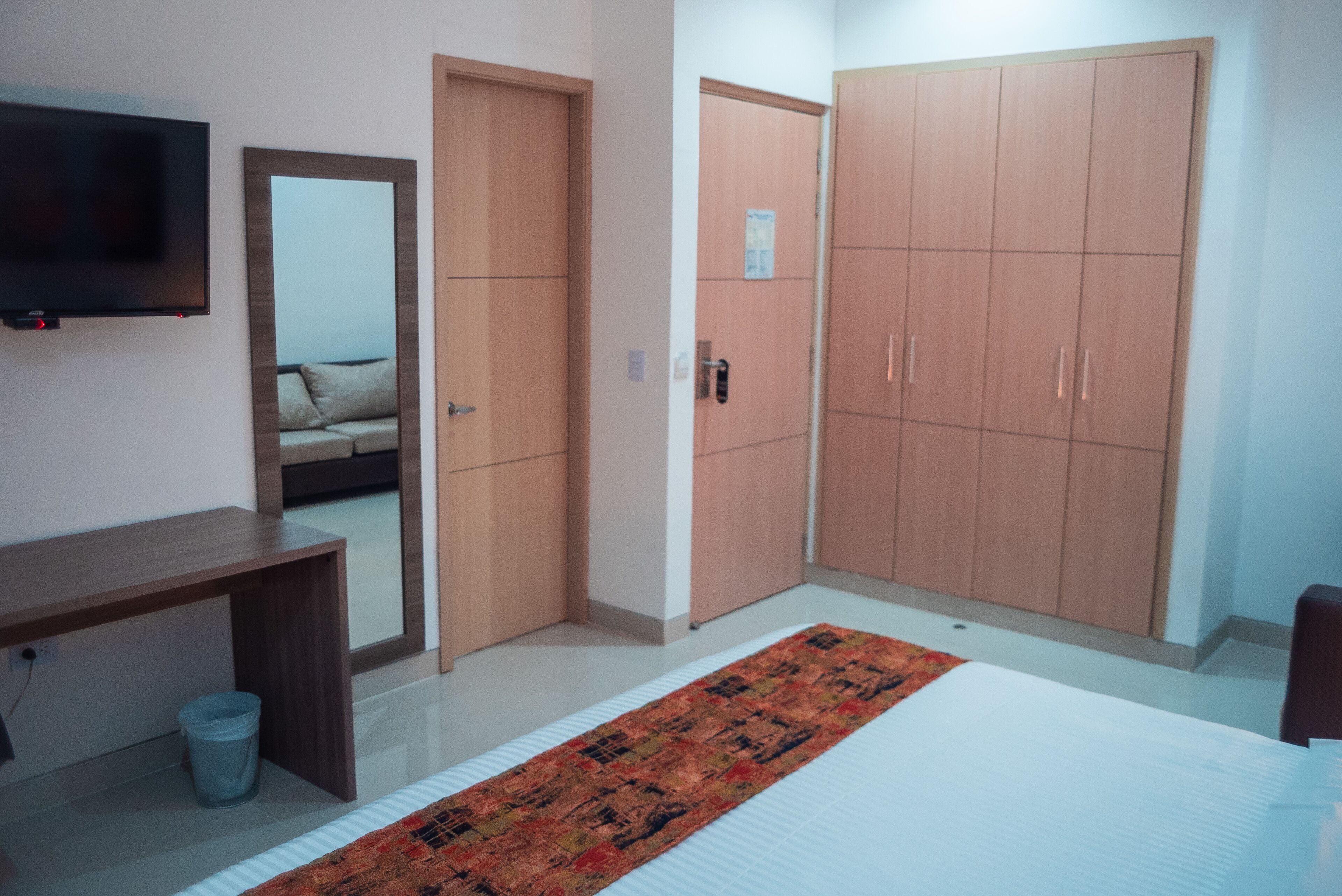 A bedroom with a bed, a TV, a mirror, a wardrobe, and a small trash bin.