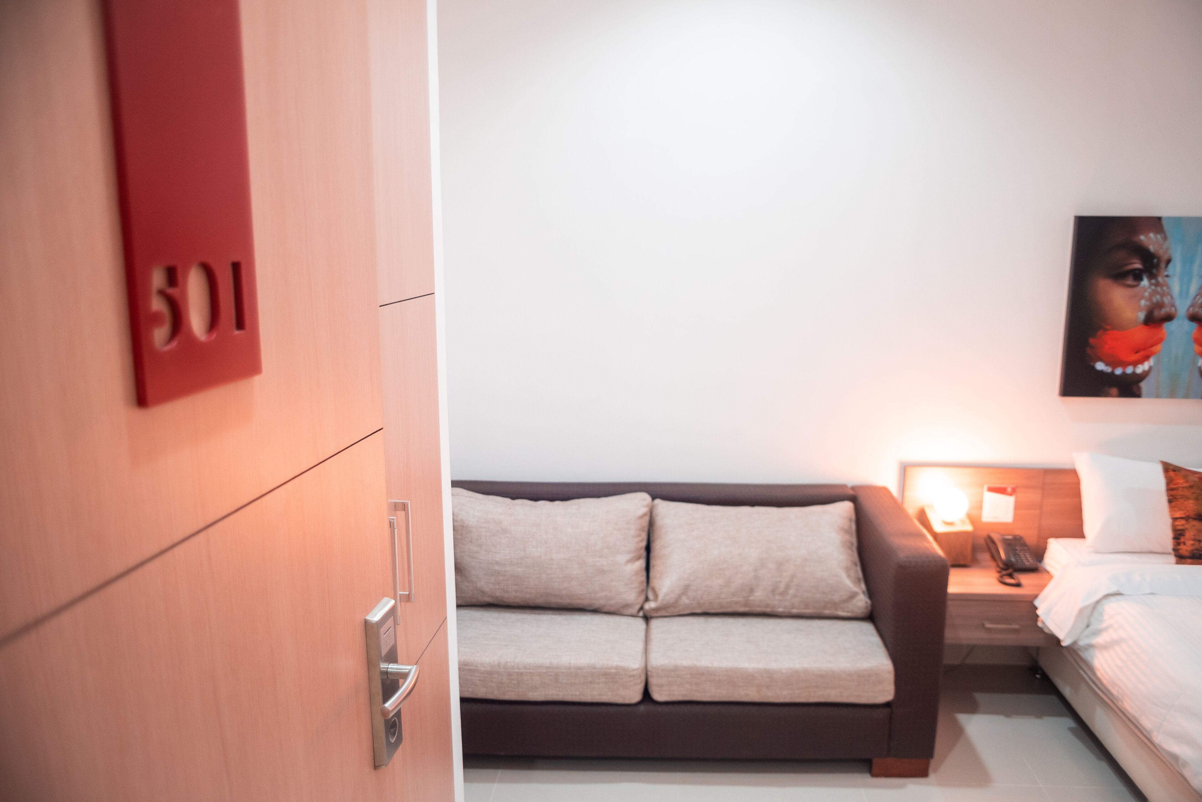 Une chambre d’hôtel avec une porte en bois portant l’inscription « 501 », un canapé, une table de chevet avec une lampe et un lit.