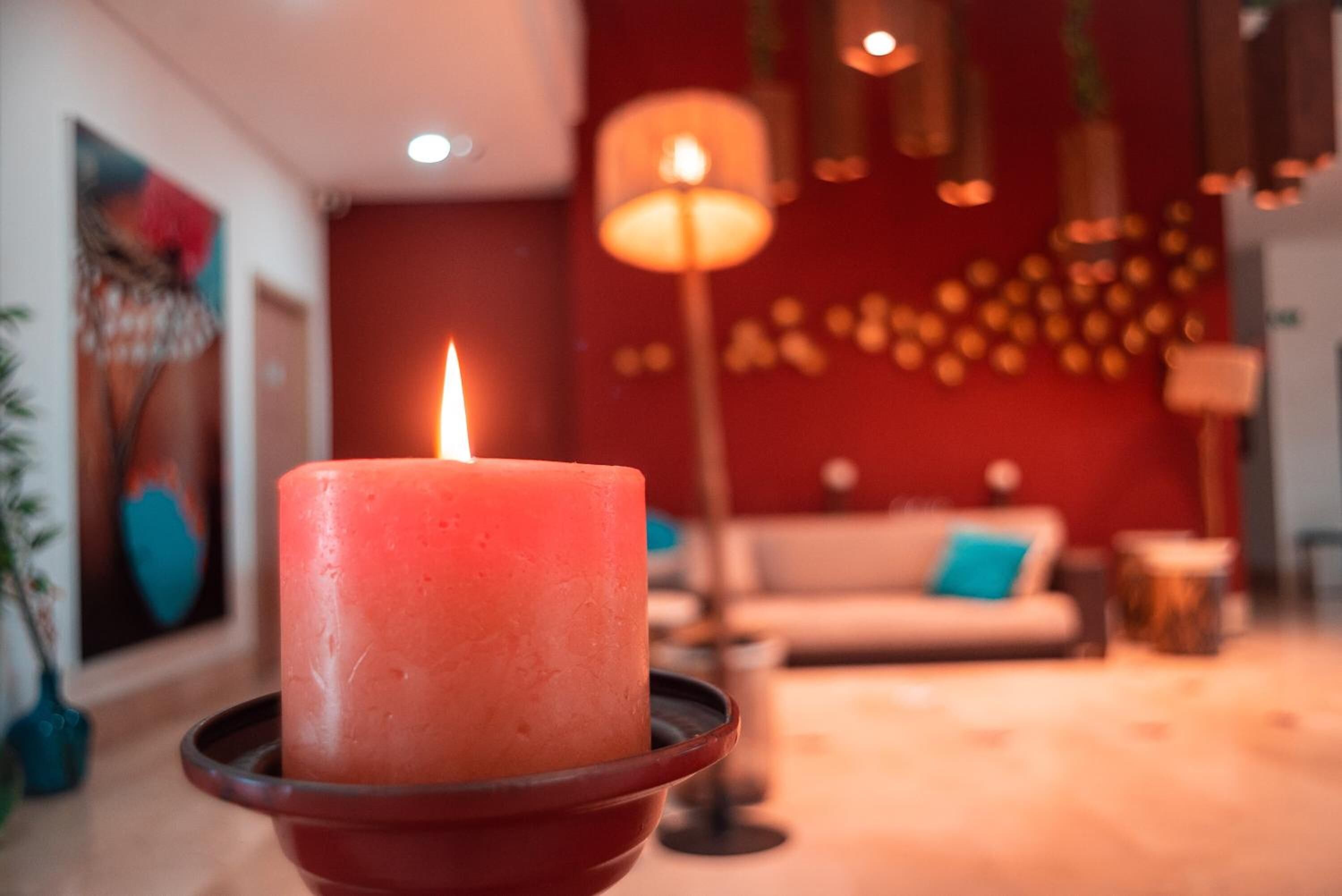 Ein Zimmer mit einer brennenden Kerze in einer Schale, einem Sofa und einer Lampe im Hintergrund.