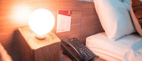 Una habitación de hotel con una lámpara de noche, un teléfono y una tarjeta de bienvenida en la pared.