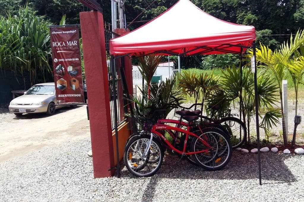 Een rode fiets staat onder een rode luifel, een witte auto en een bord met 'ROCA MAR Spa Hotel'.