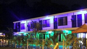 Un hotel de varios pisos con balcones iluminados y una zona de piscina con palmeras.