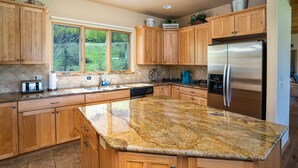 Una cocina amplia con armarios de madera, encimeras de granito, refrigerador de acero inoxidable y un ventanal con vistas a la vegetación.