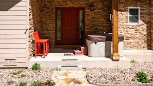 Una casa con fachada de piedra, una puerta roja y un porche cubierto con una silla roja y un jacuzzi.