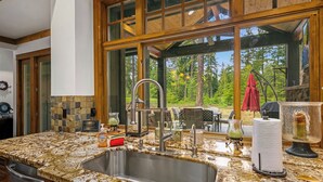 A kitchen with a granite countertop, stainless steel sink, and large windows overlooking a forest. - Evergreen Escape Estates with lots of amenities ! AVAILABLE FOR LONG TERM  (Cle Elum)