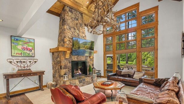 A spacious living room with a stone fireplace, leather sofas, a large window with a view of greenery, and a mounted television. - Evergreen Escape Estates with lots of amenities ! AVAILABLE FOR LONG TERM  (Cle Elum)