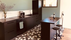 Eine moderne Küche mit dunklen Schränken, einer Kaffeemaschine und einer Weinflasche auf der Arbeitsplatte.