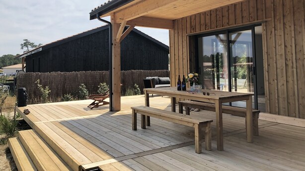 Eine Holzdachterrasse mit Tisch und Bänken, eine große Schiebeglastür und ein Holzzaun im Hintergrund.