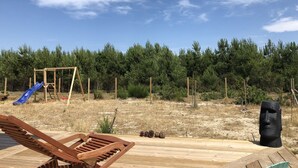 Eine Holzterrasse mit Liegestuhl, Schaukel und Statue.