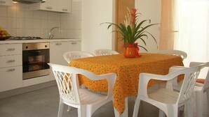 Una cocina compacta con armarios blancos, horno integrado y comedor con mesa lista para cuatro.