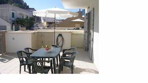 Un patio al aire libre con una mesa, sillas, un florero y sombrillas.