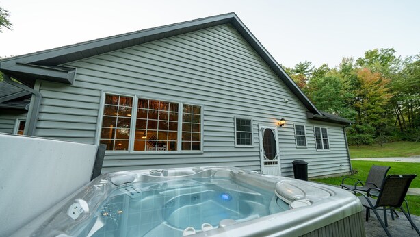 Une maison avec un jacuzzi à l’avant, une pelouse et un chemin menant à la maison.