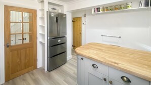 Une cuisine avec une porte en bois, un réfrigérateur en acier inoxydable, un plan de travail en bois et une étagère remplie de bocaux.