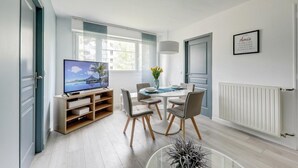 A modern living room with a flat-screen TV, a dining table with chairs, a vase with flowers, and a framed quote on the wall. - Apartment coup de coeur, 3 bedrooms, 10 minutes from Rouen, Netflix (Mont-Saint-Aignan)