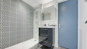 A modern bathroom with a geometric patterned wall, a built-in shower, and a blue door. - Apartment coup de coeur, 3 bedrooms, 10 minutes from Rouen, Netflix (Mont-Saint-Aignan)